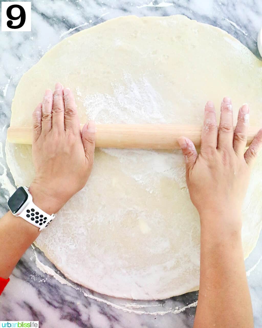 hands using a rolling pin to roll out homemade pie dough on a marble countertop.