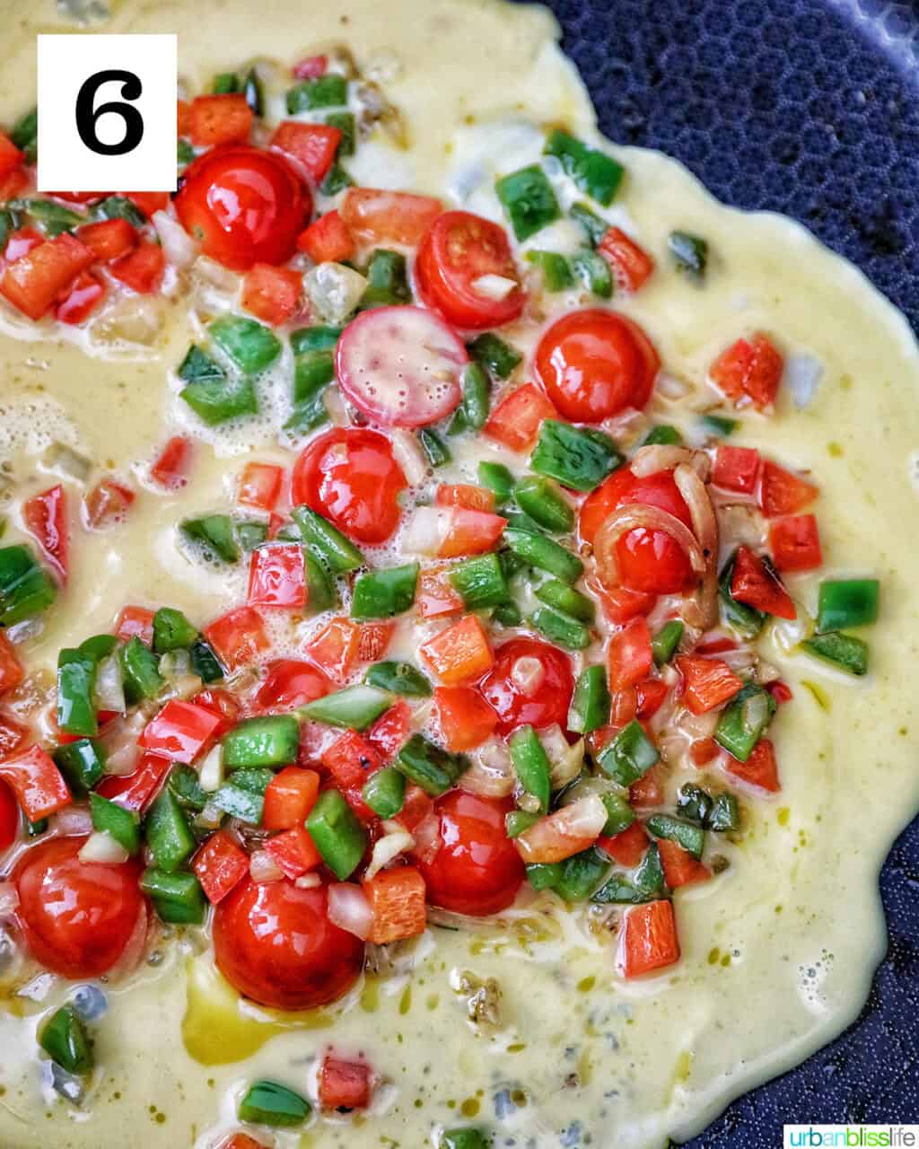 eggs with cherry tomatoes, garlic, onions, red bell peppers and green bell peppers in a skillet.