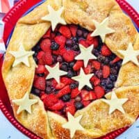 a mixed berry galette: mixed berries in pie dough with white chocolate stars on a red plate.