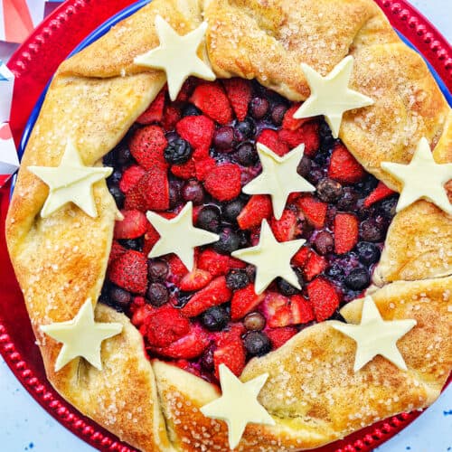 a mixed berry galette: mixed berries in pie dough with white chocolate stars on a red plate.