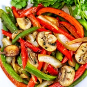 sautéed peppers and onions in a white bowl with garnish of parsley.