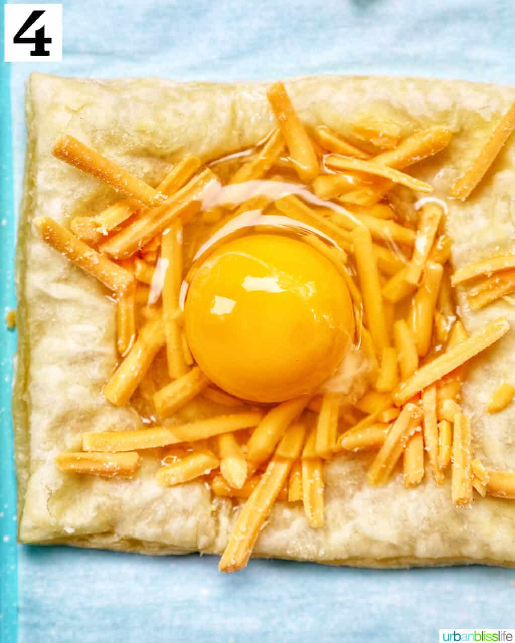 egg on top of shredded cheddar cheese on puff pastry.