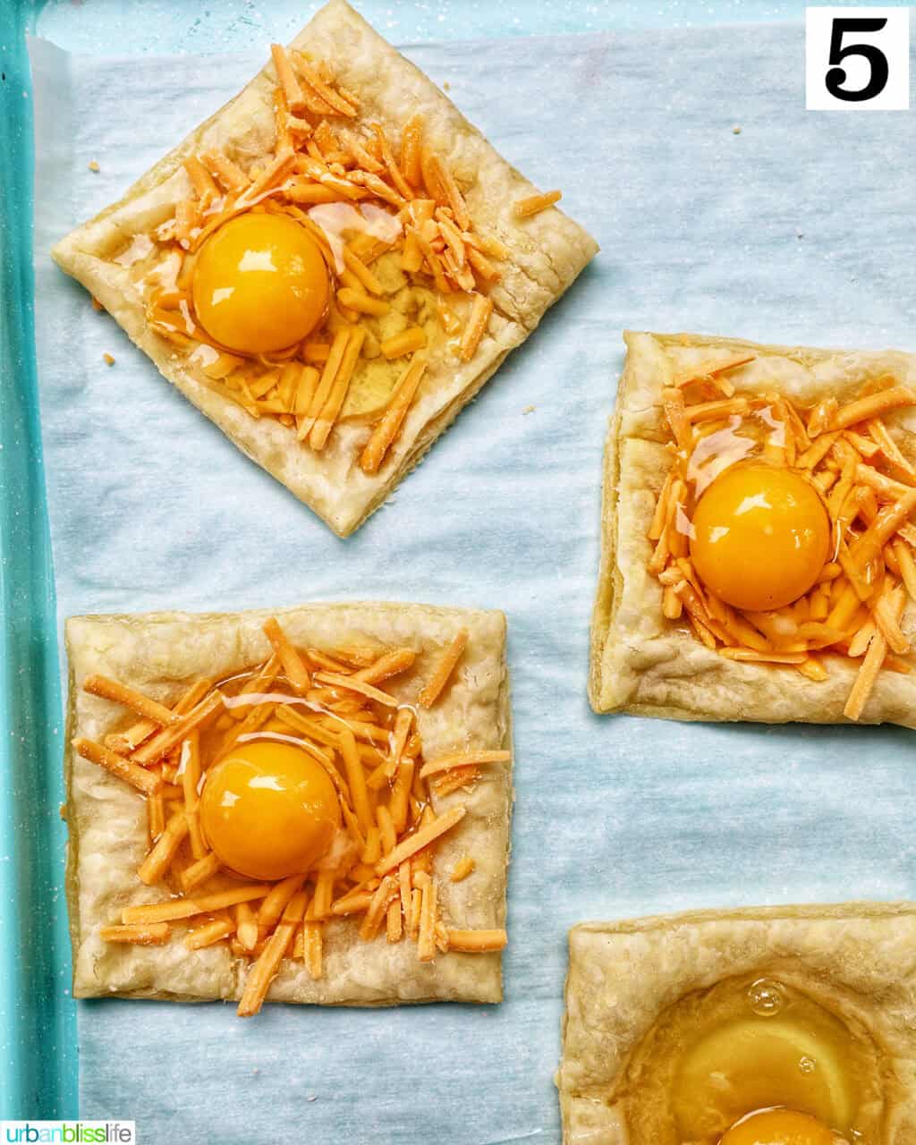 puff pastry squares with eggs and cheese on top, on a baking sheet.