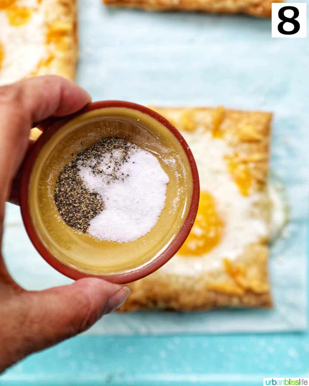 hand holding bowl of salt and pepper over eggs in puff pastry.
