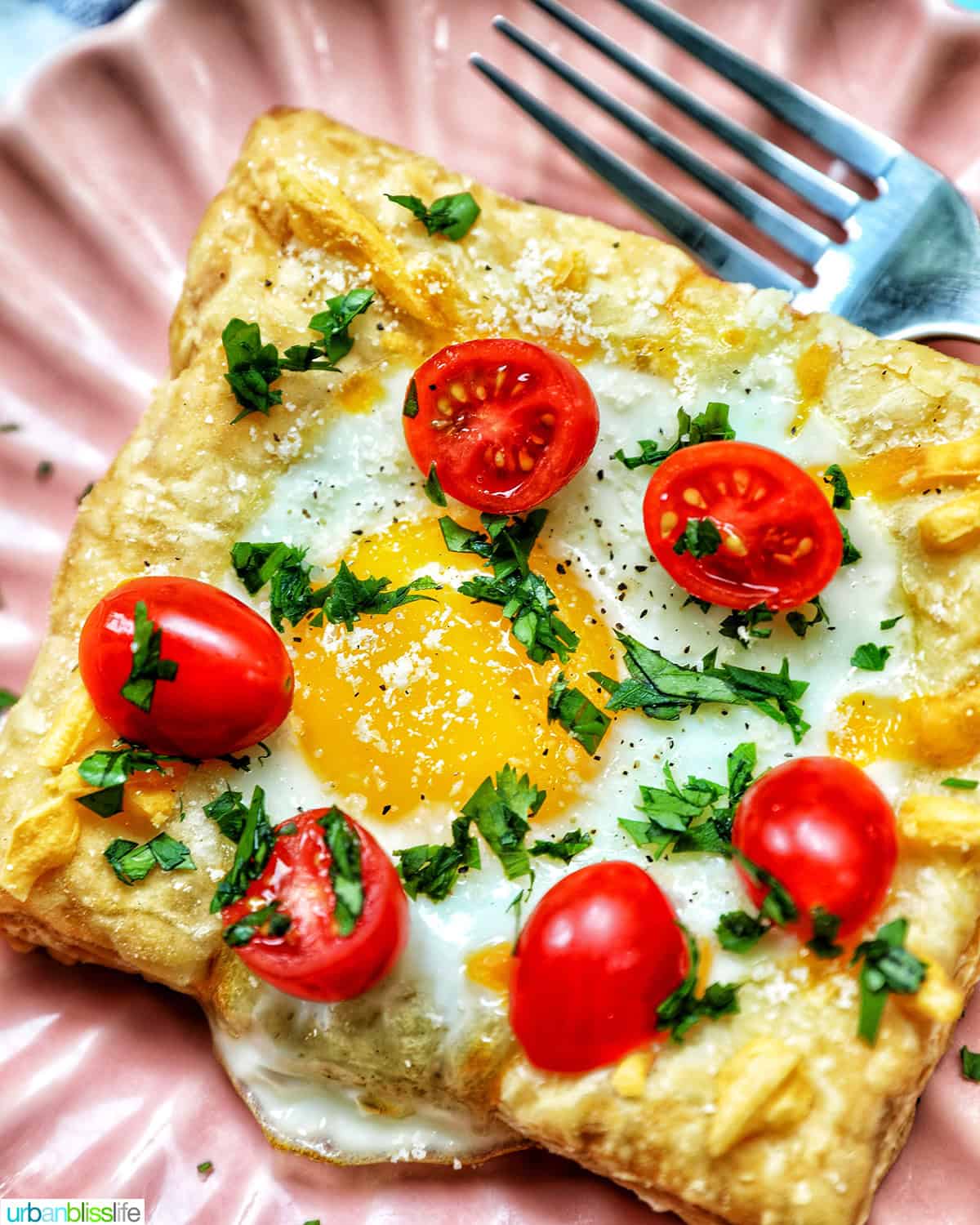 egg in puff pastry on a plate with tomatoes and parsley garnish.