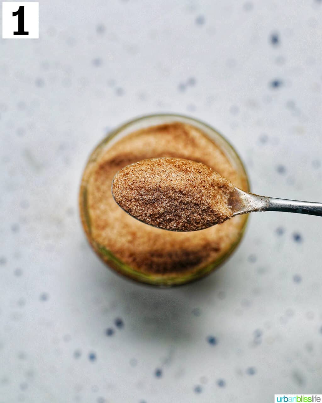 spoon holding cinnamon sugar above a mason jar of cinnamon sugar.