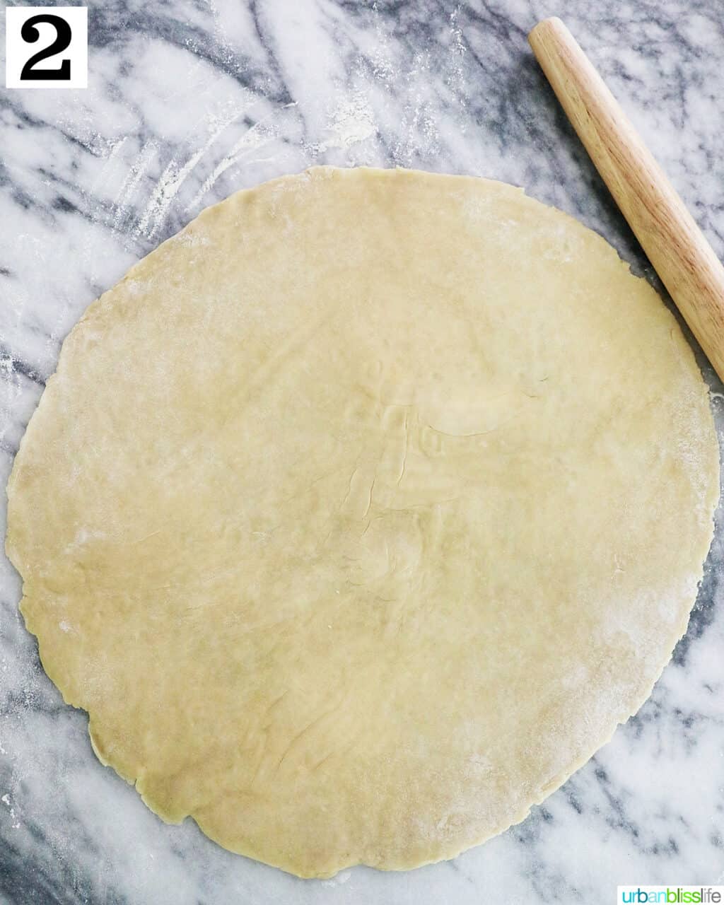 rolled out homemade pie dough on marble next to a rollng pin.