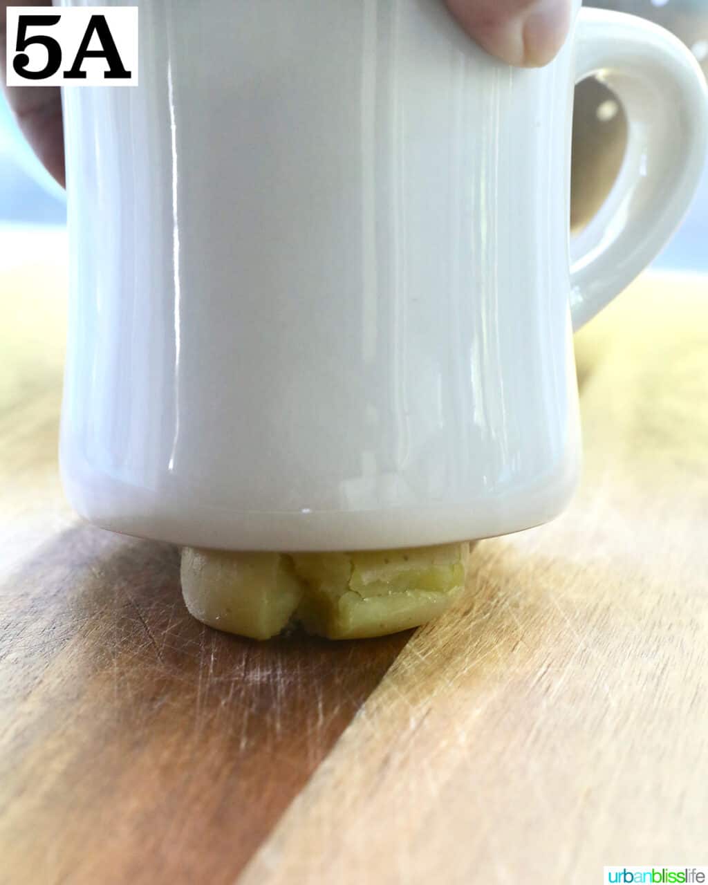 white mug smashing down on a baby potato on a cutting board.