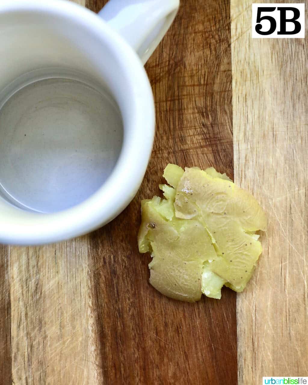 white mug next to a single smashed potato on a cutting board.