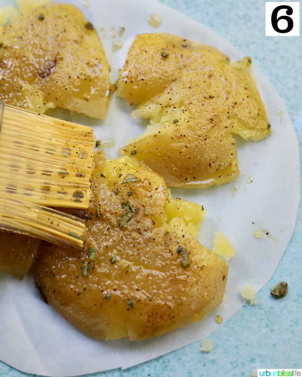 pastry brush brushing olive oil herb mixture onto smashed potatoes.