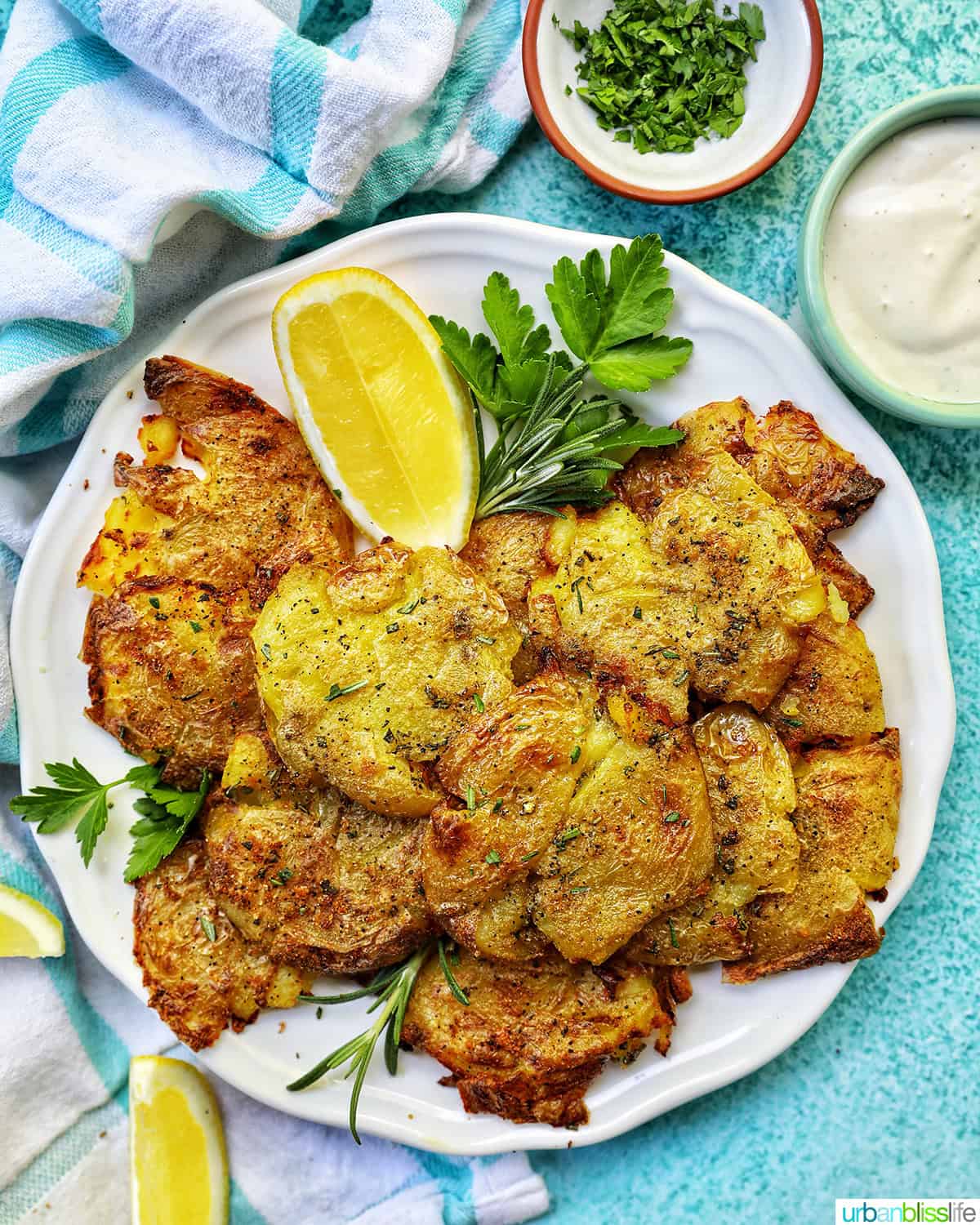 smashed potatoes on a plate with sides of lemon edges and herbs and sauce.