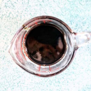 measuring cup of balsamic glaze on a blue background.