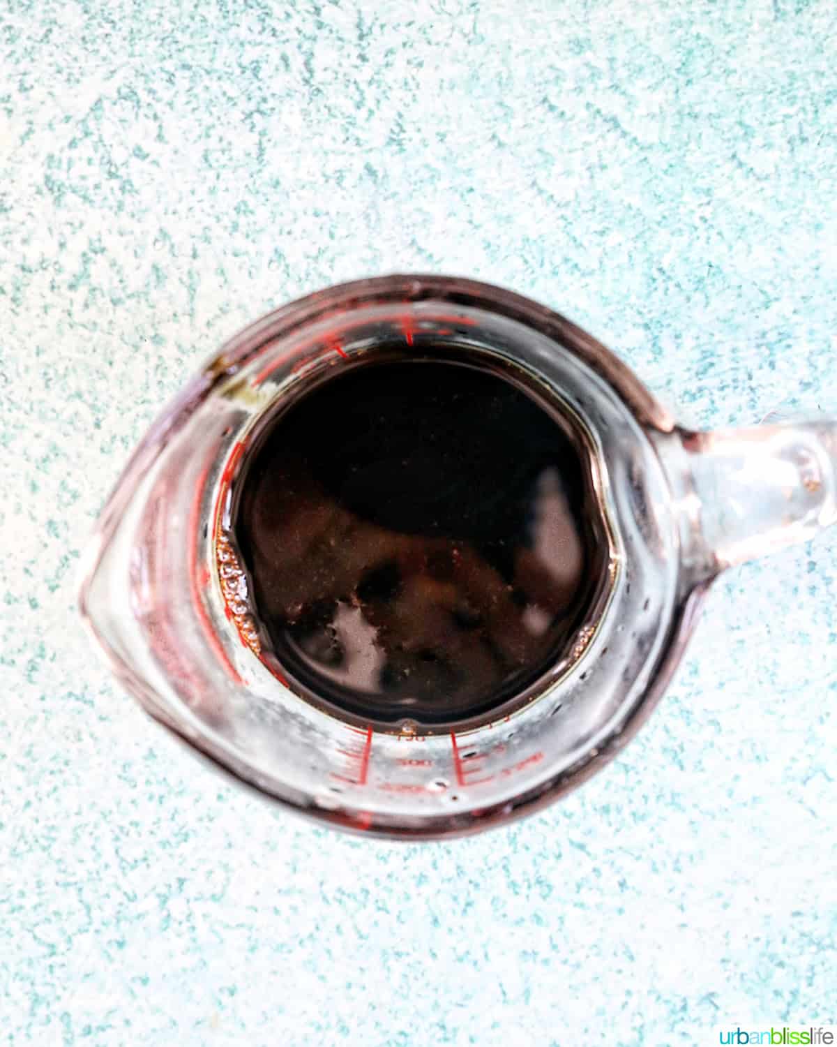 measuring cup of balsamic glaze on a blue background.
