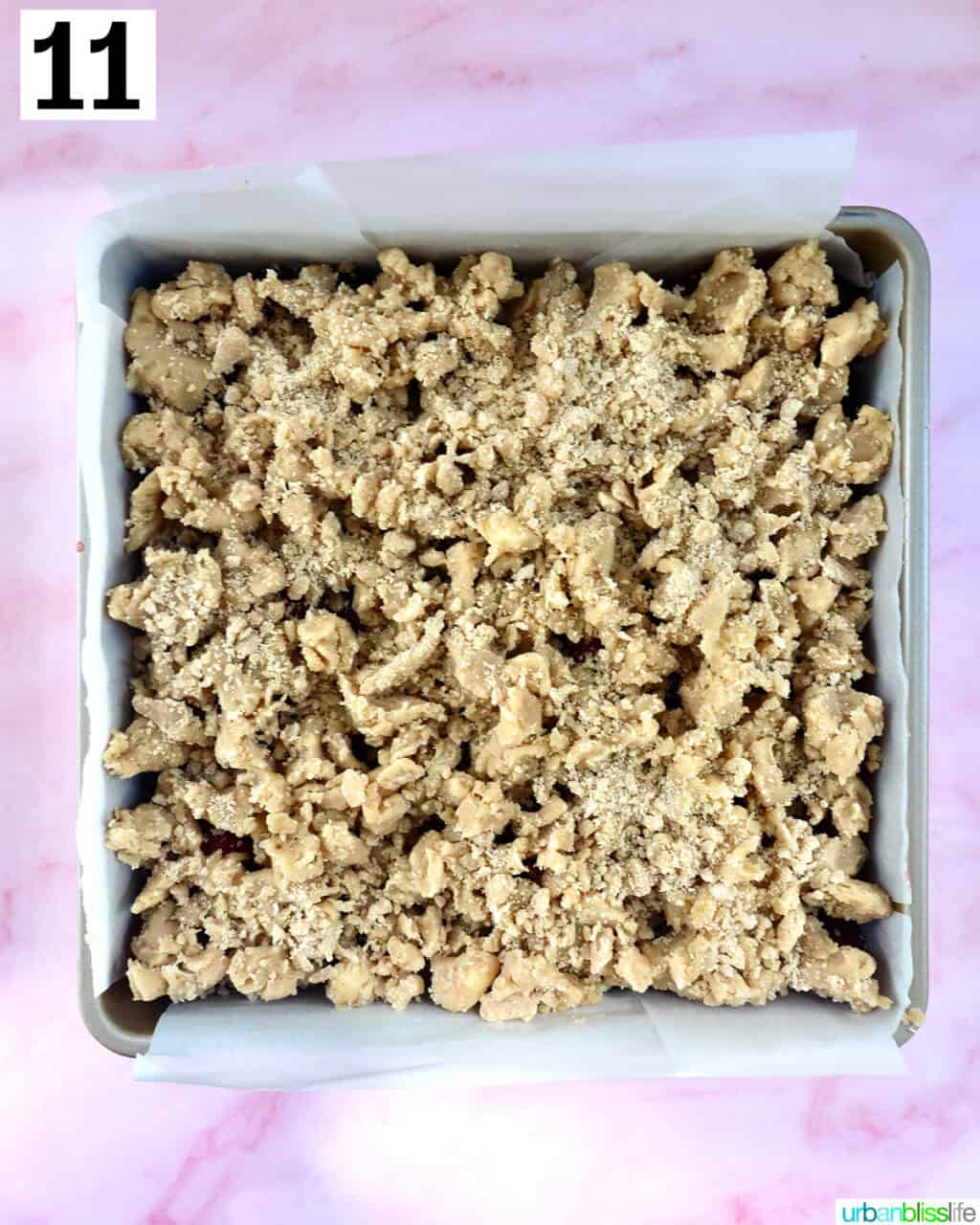 crumb topping added to cherry crumb bars in a baking dish.