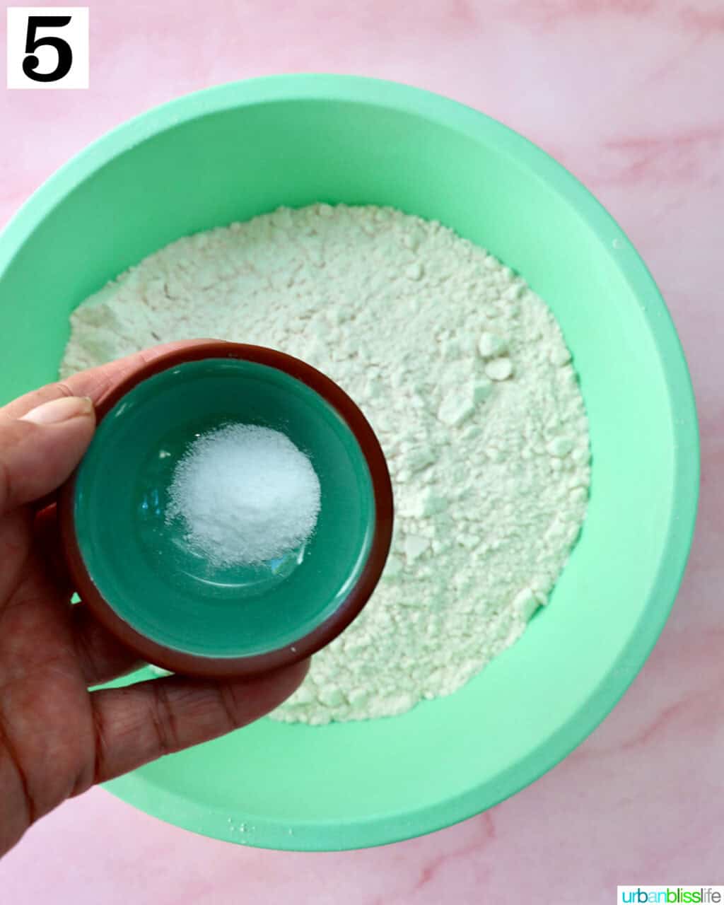 hand holding a small bowl of salt over a large green bowl with flour.