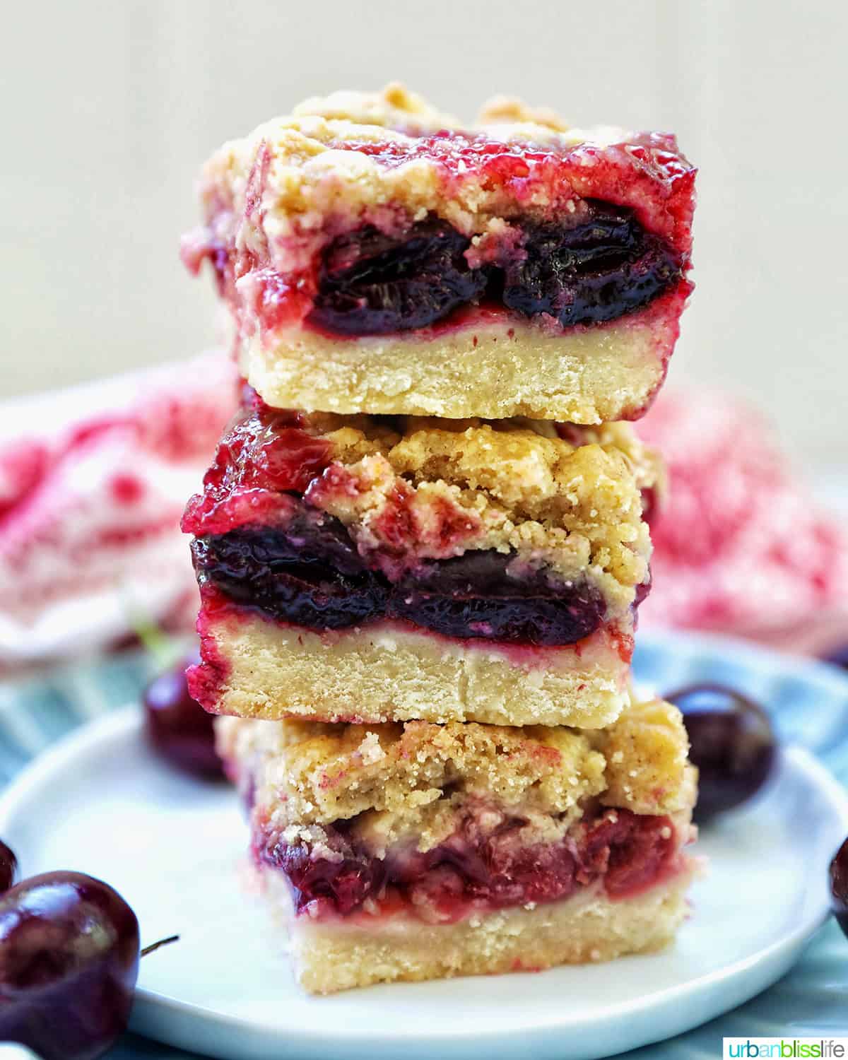 stack of three cherry crumble bars on a plate surrounded by cherries.