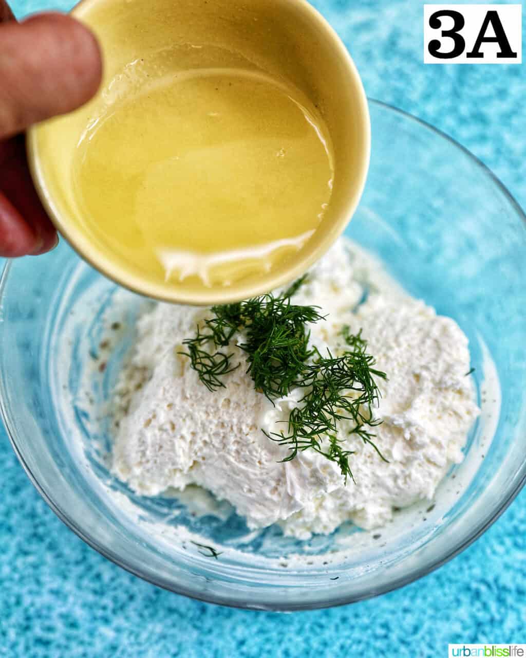 hand pouring lemon juice into herb cream cheese spread in a bowl.