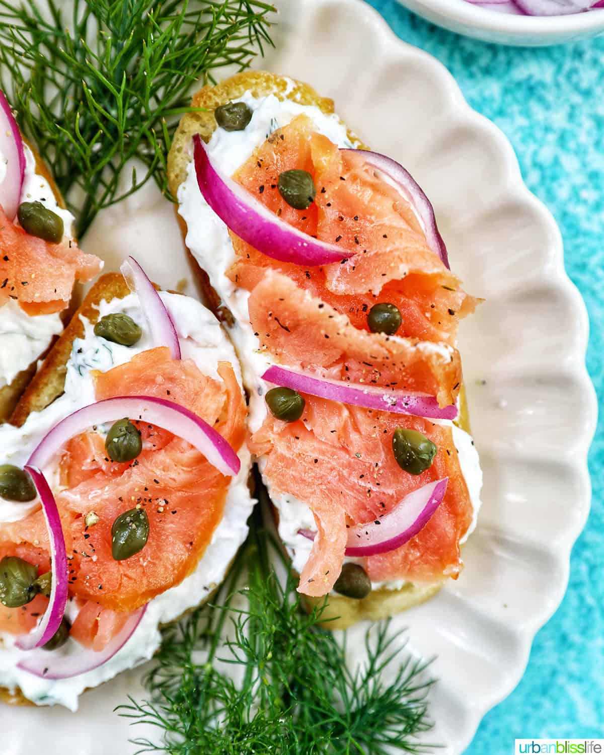 plate with two salmon crostini, side of red onion slices, and lemon wedges and dill sprigs as garnish.