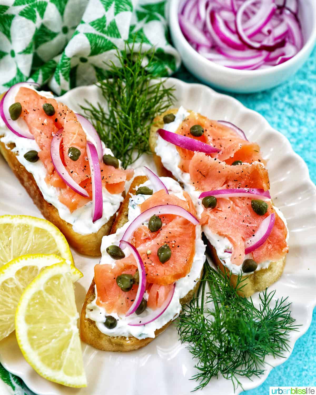 plate with three salmon crostini, side of red onion slices, and lemon wedges and dill sprigs as garnish.