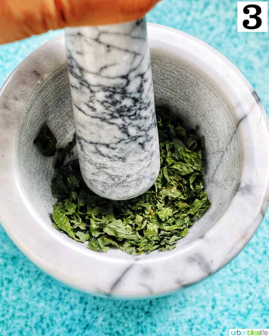 dried oregano leaves being crushed in a marble bowl.