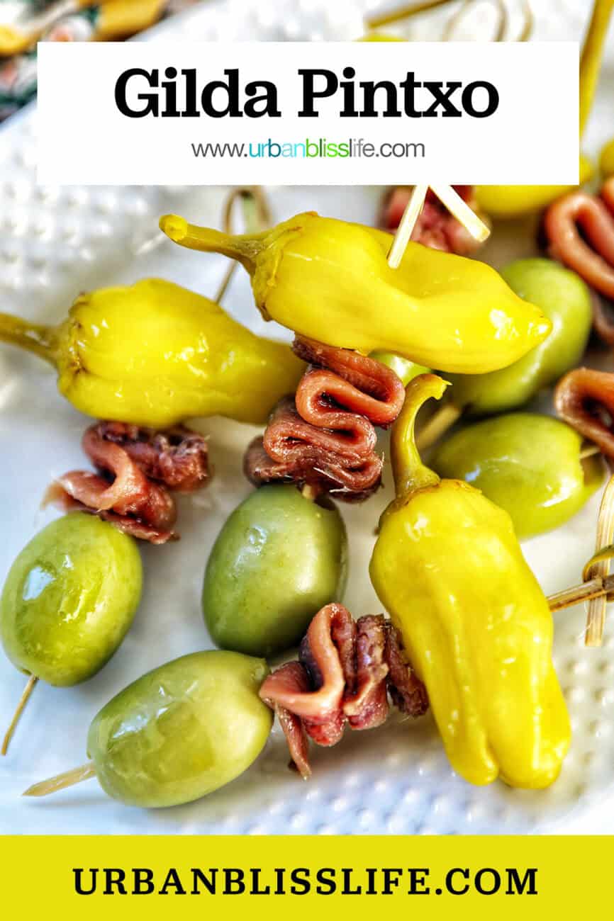 Gilda pintxos: food sticks with peppers, anchovies, and olives on a white plate.