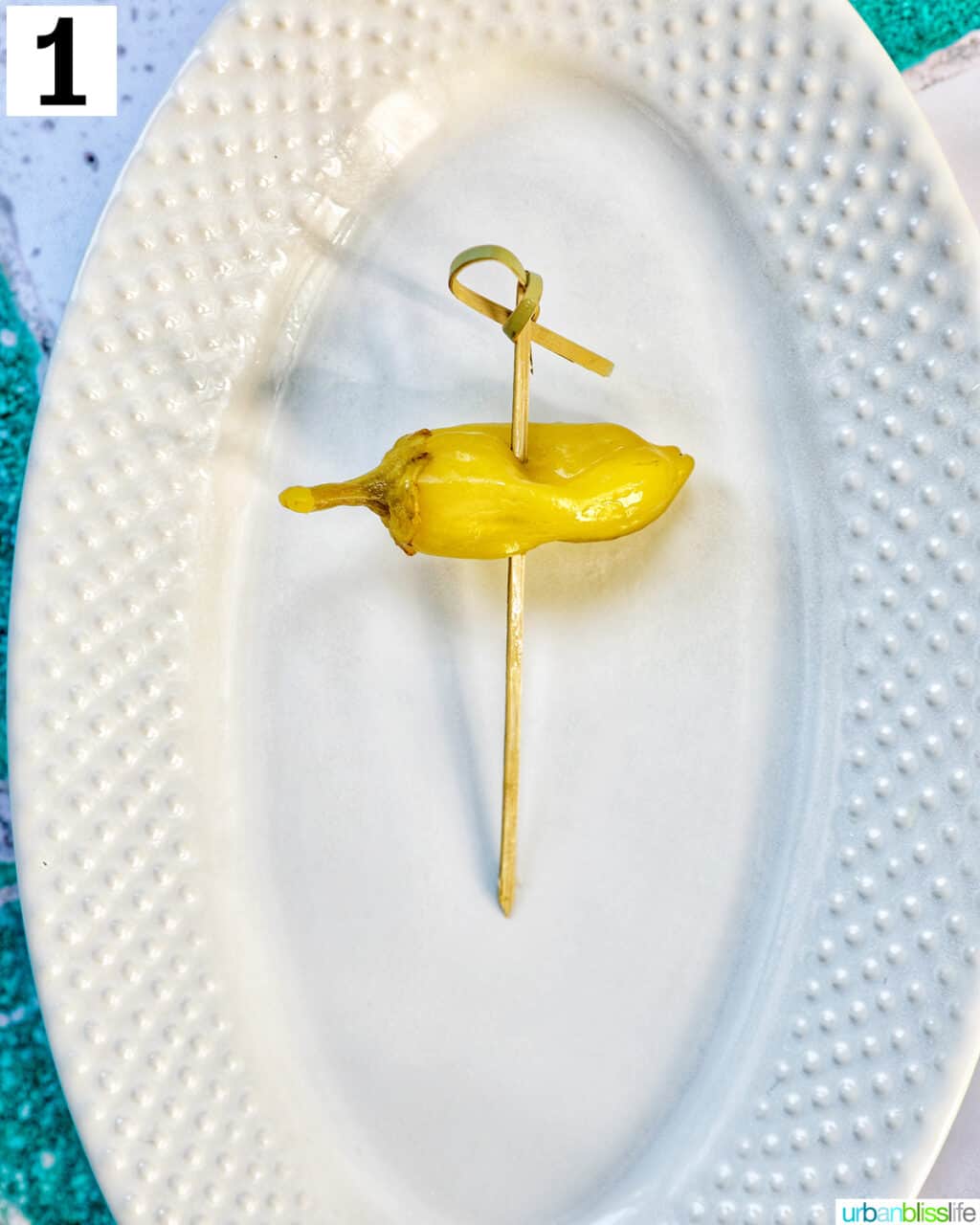 white plate with a single food pick with pepper.