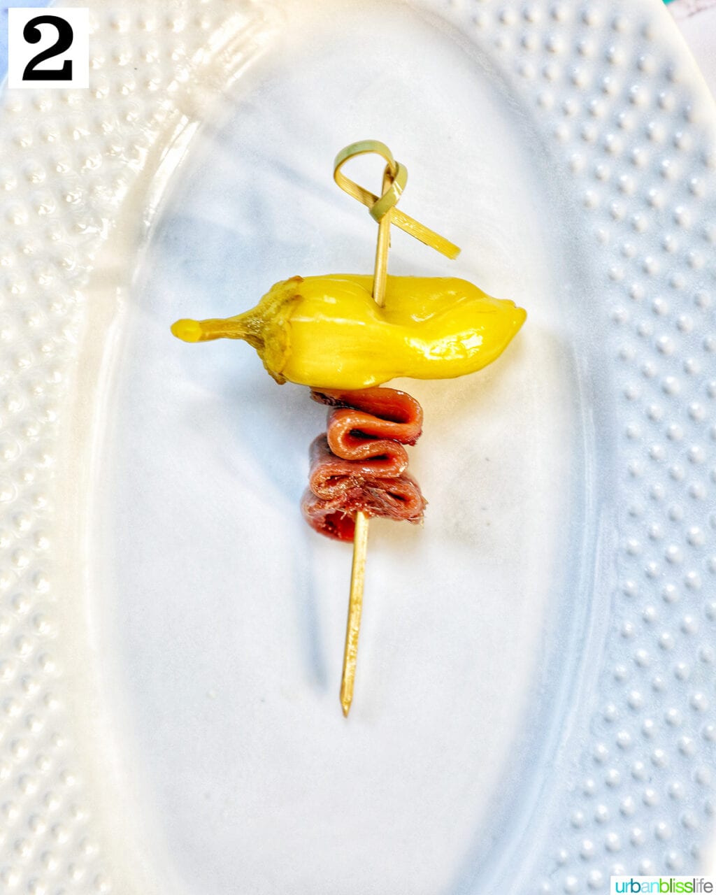 white plate with a single food pick with pepper and anchovy.