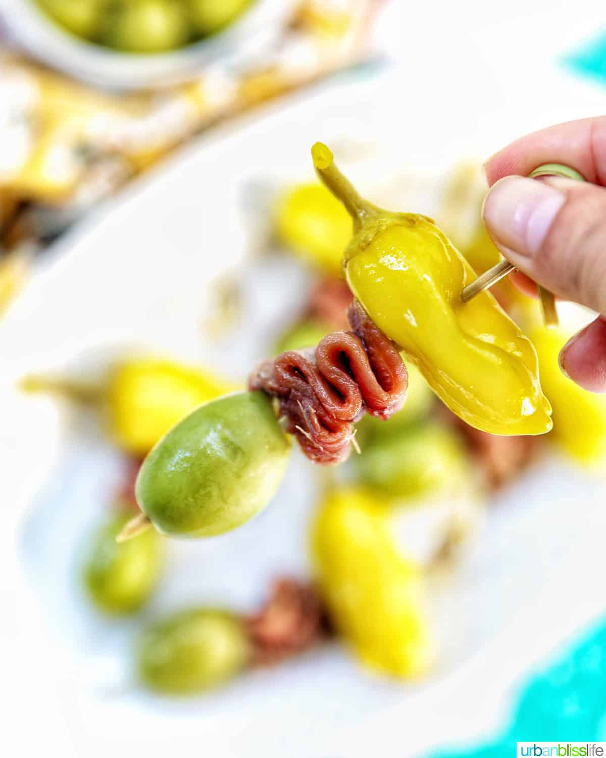 hand holding a single Gilda pintxo above a plate of Gilda pintxos.