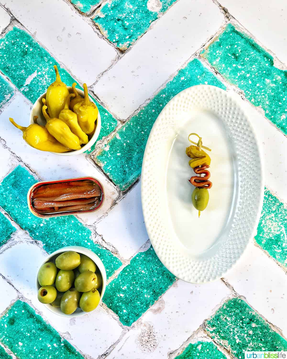 bowls of peppers, anchovies, olives next to a plate with a single Gilda pintxo on it.