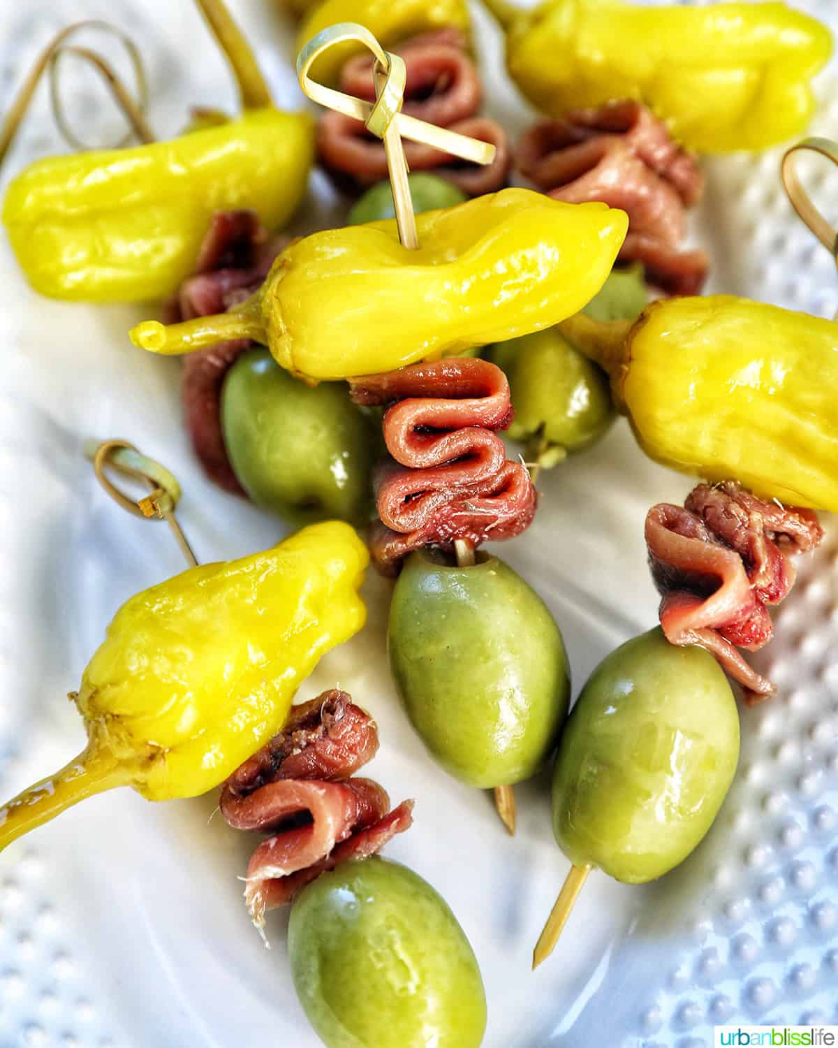 Gilda pintxos: food sticks with peppers, anchovies, and olives on a white plate.