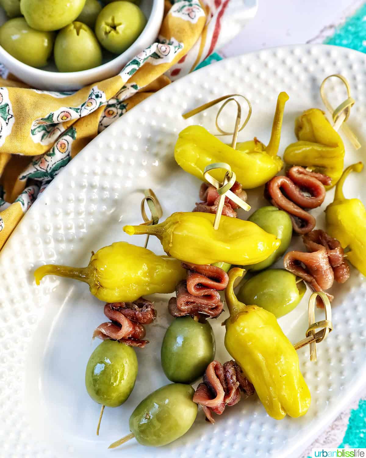 Gilda pintxos: food sticks with peppers, anchovies, and olives on a white plate.