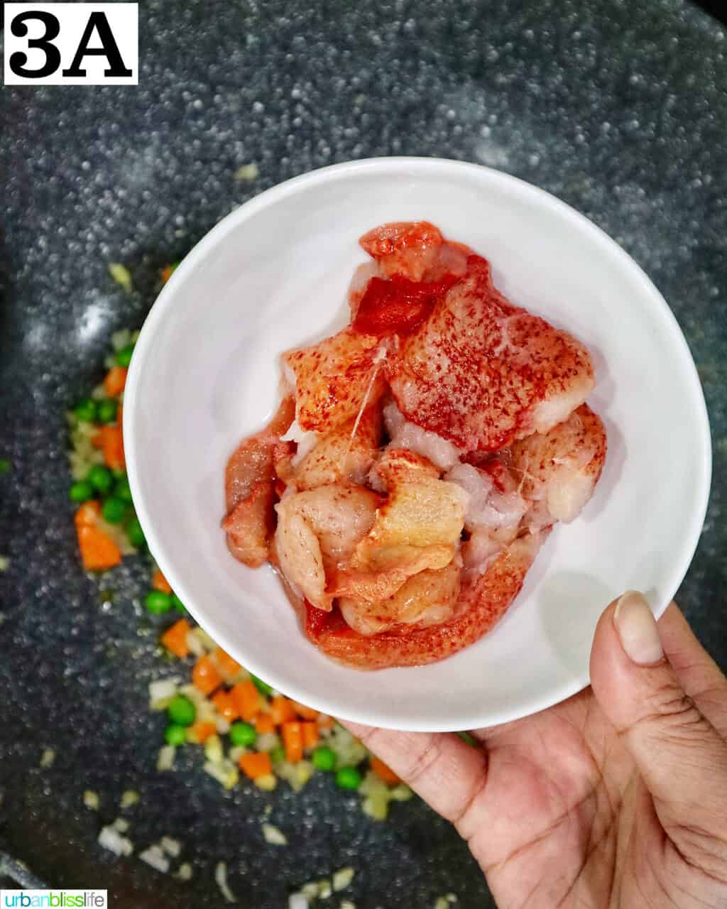 hand holding a bowl of lobster meat over a wok.