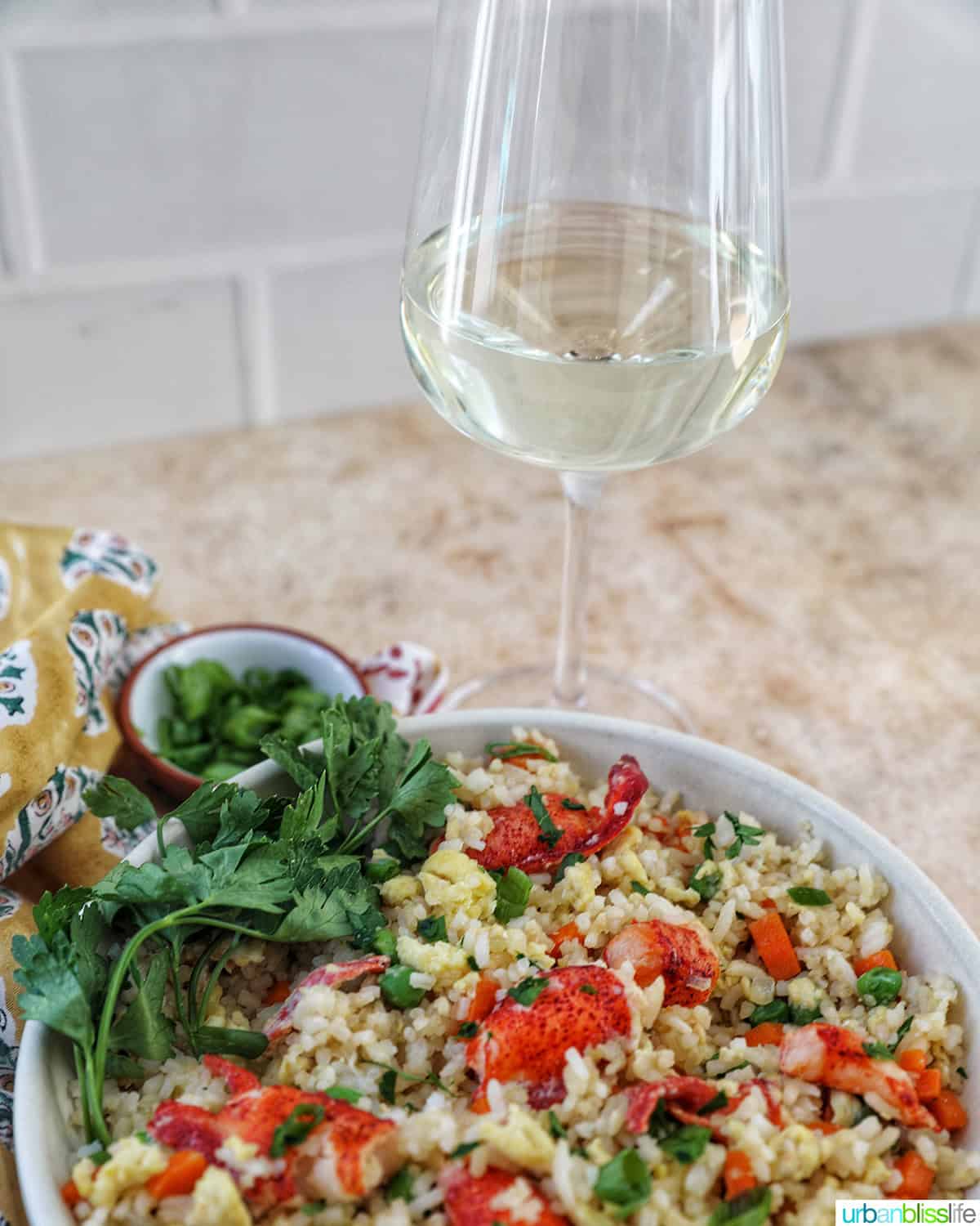 bowl of lobster fried rice with bowls of fresh herbs and a glass of white wine.
