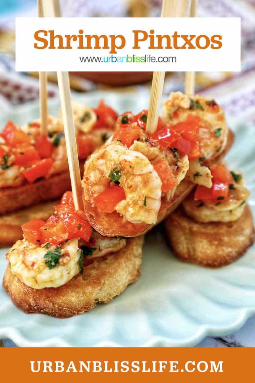 shrimp pintxos skewers with tomatoes on crostini bread on a scalloped plate with title text overlay.