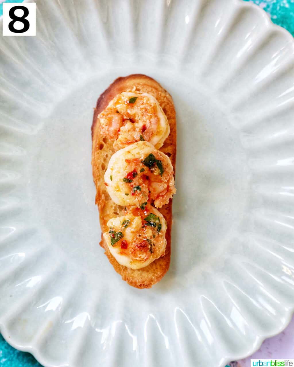 shrimp on sliced baguette bread on a scalloped plate.