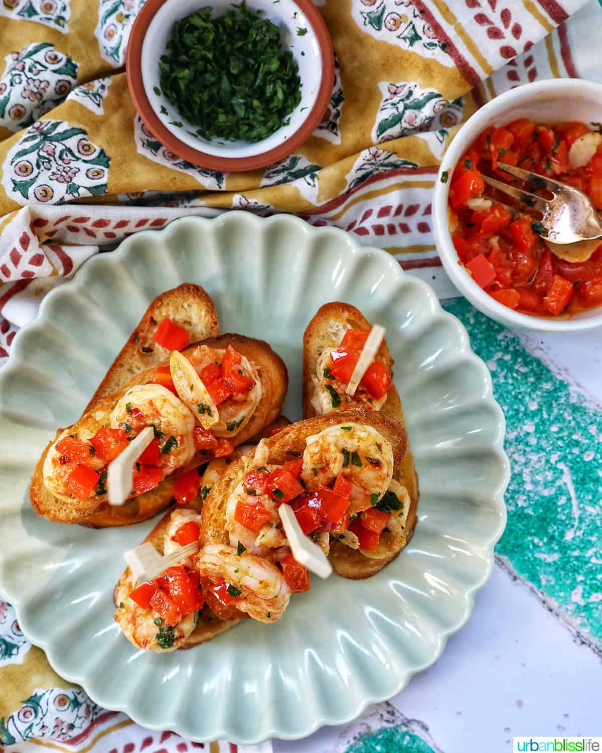 shrimp pintxos skewers with tomatoes on crostini bread on a scalloped plate.