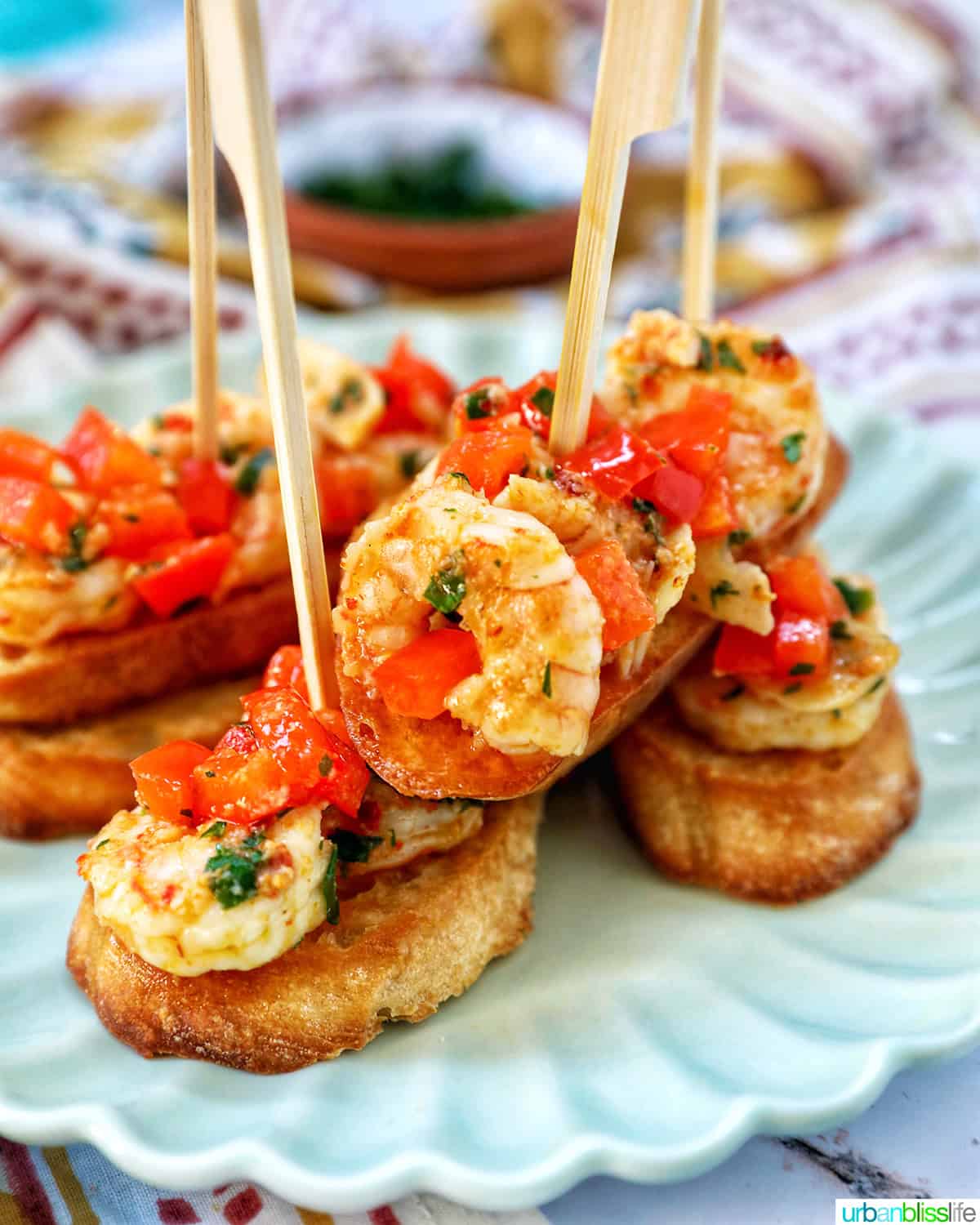 shrimp pintxos skewers with tomatoes on crostini bread on a scalloped plate.