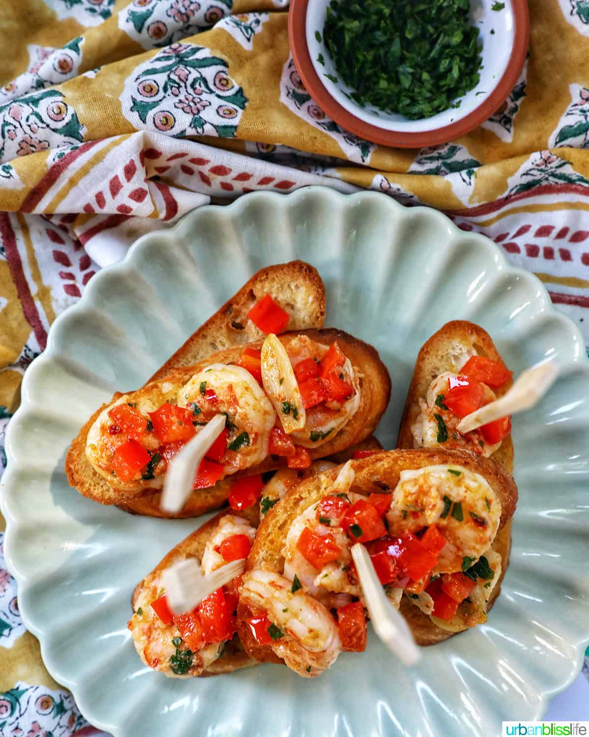 shrimp pintxos skewers with tomatoes on crostini bread on a scalloped plate.