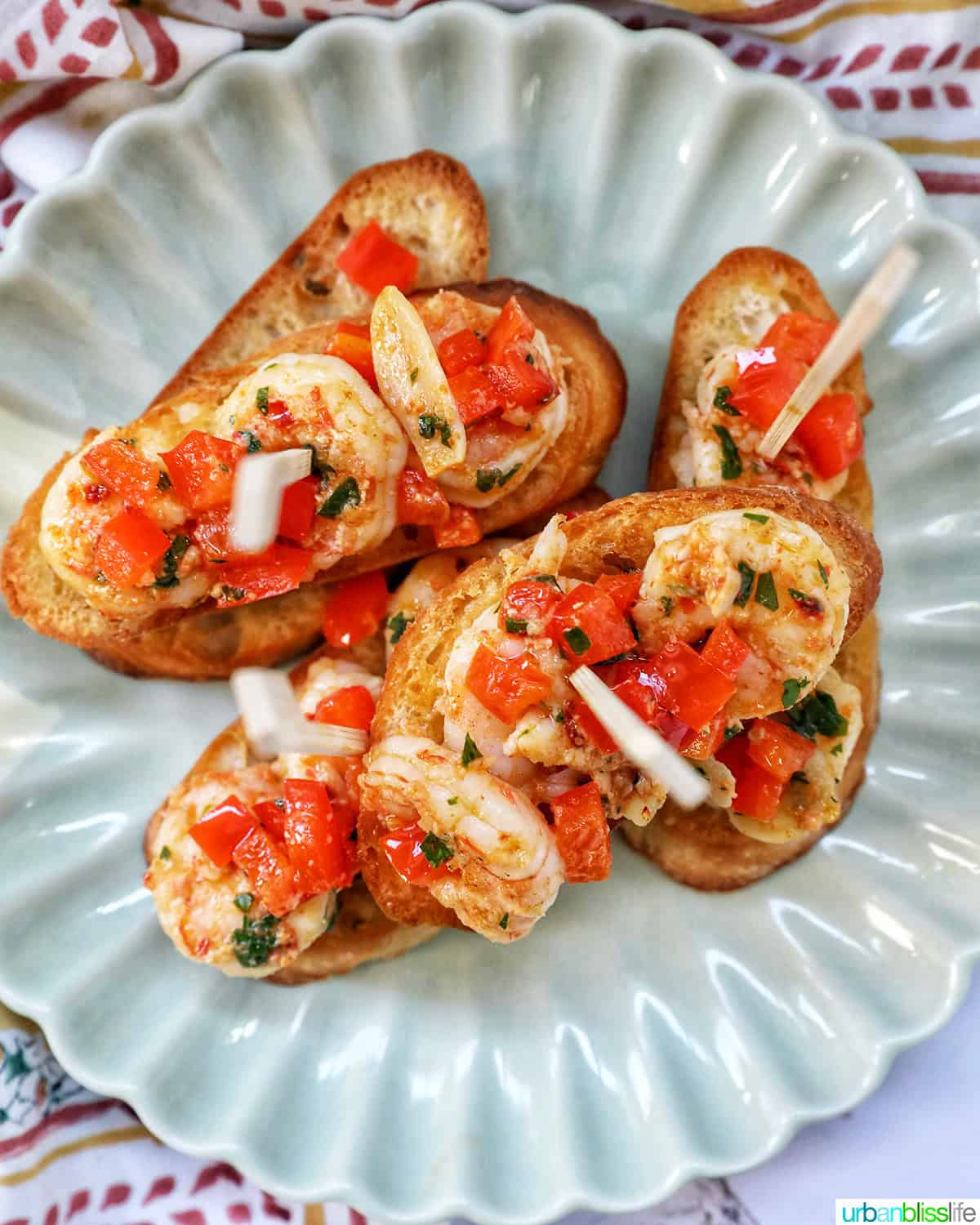 shrimp pintxos skewers with tomatoes on crostini bread on a scalloped plate.