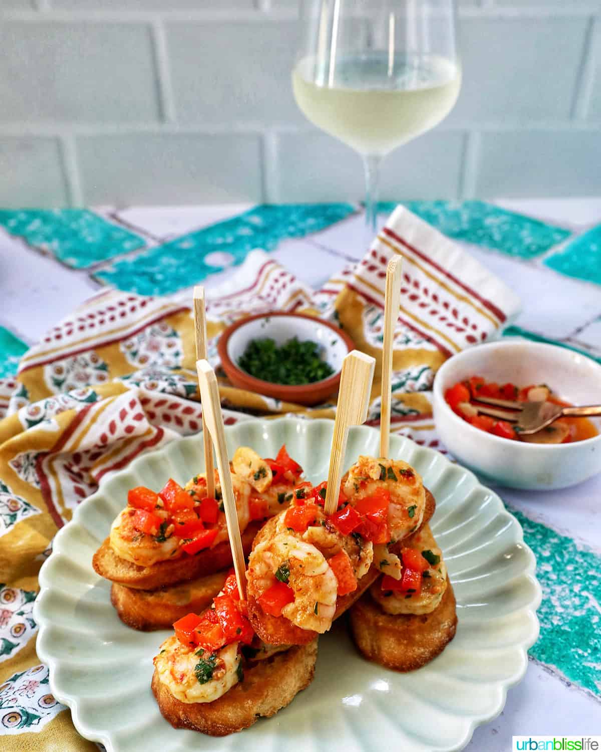 shrimp pintxos skewers with tomatoes on crostini bread on a scalloped plate with a glass of white wine.