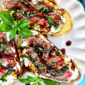 steak crostini with fresh basil leaves as garnish on a plate.