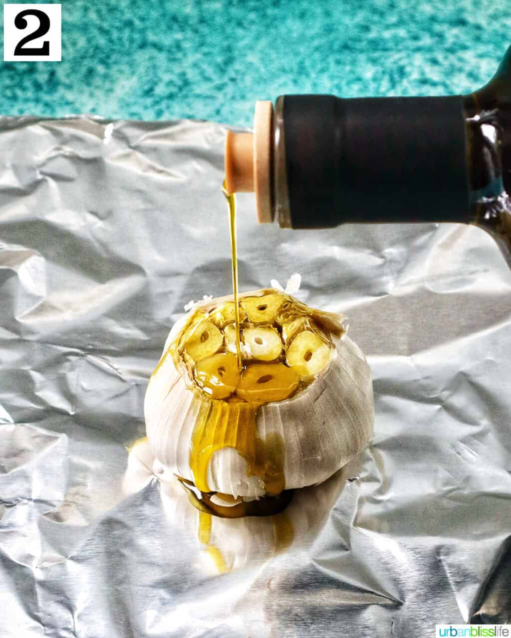 olive oil drizzling over garlic head on aluminum foil.