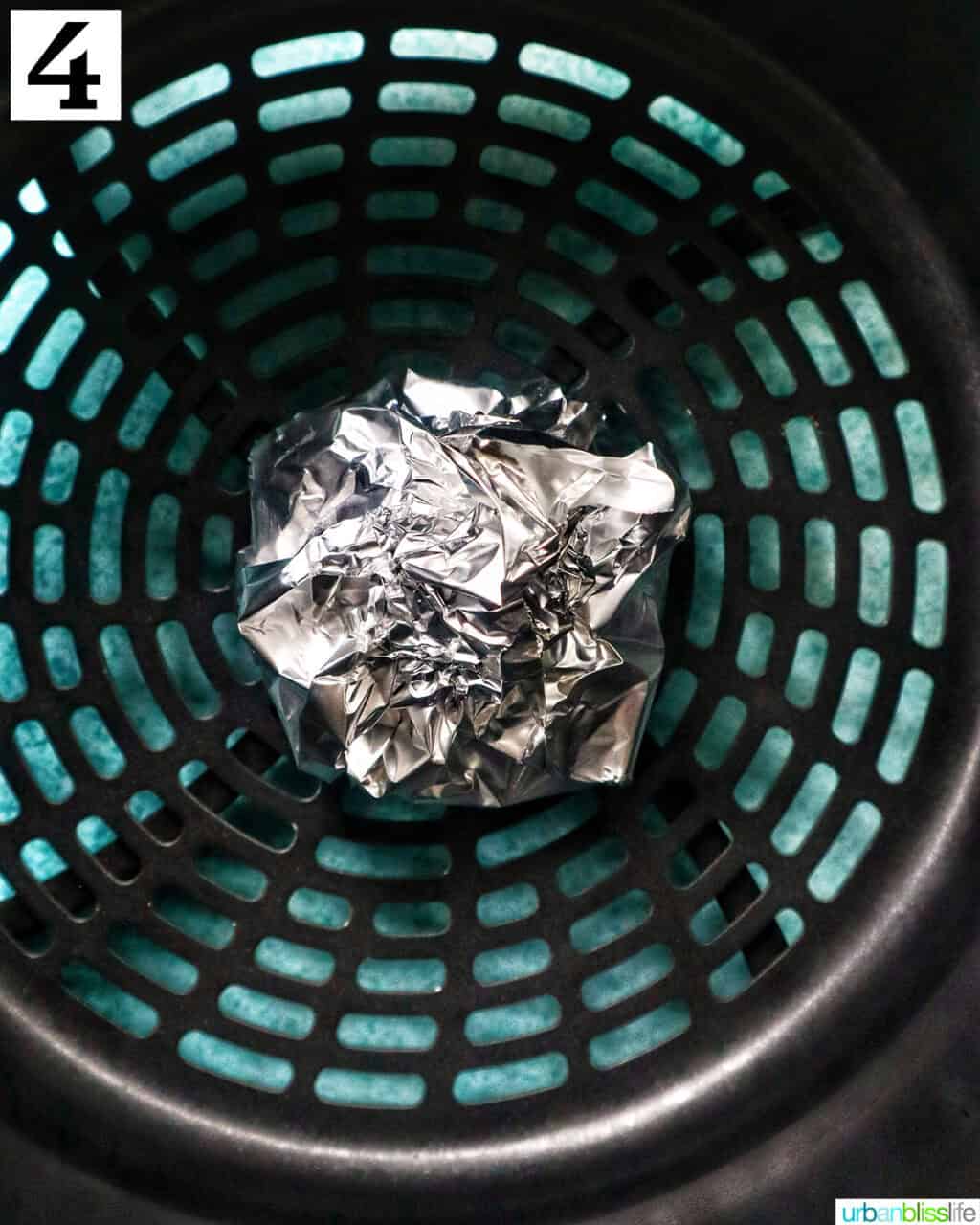 aluminum foil pack of garlic head in an air fryer basket.