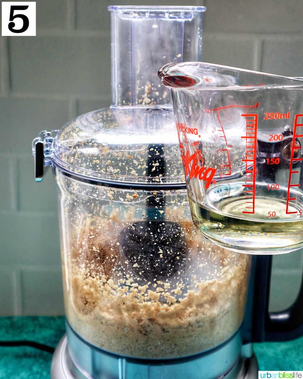 measuring cup with oil next to a food processor with tahini.