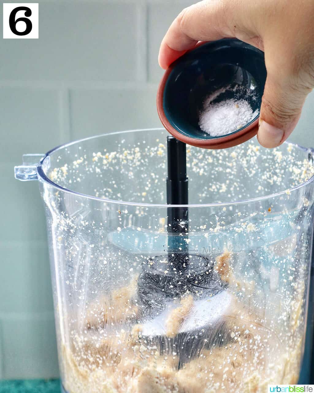 hand holding salt over a food processor with sesame seeds making tahini.