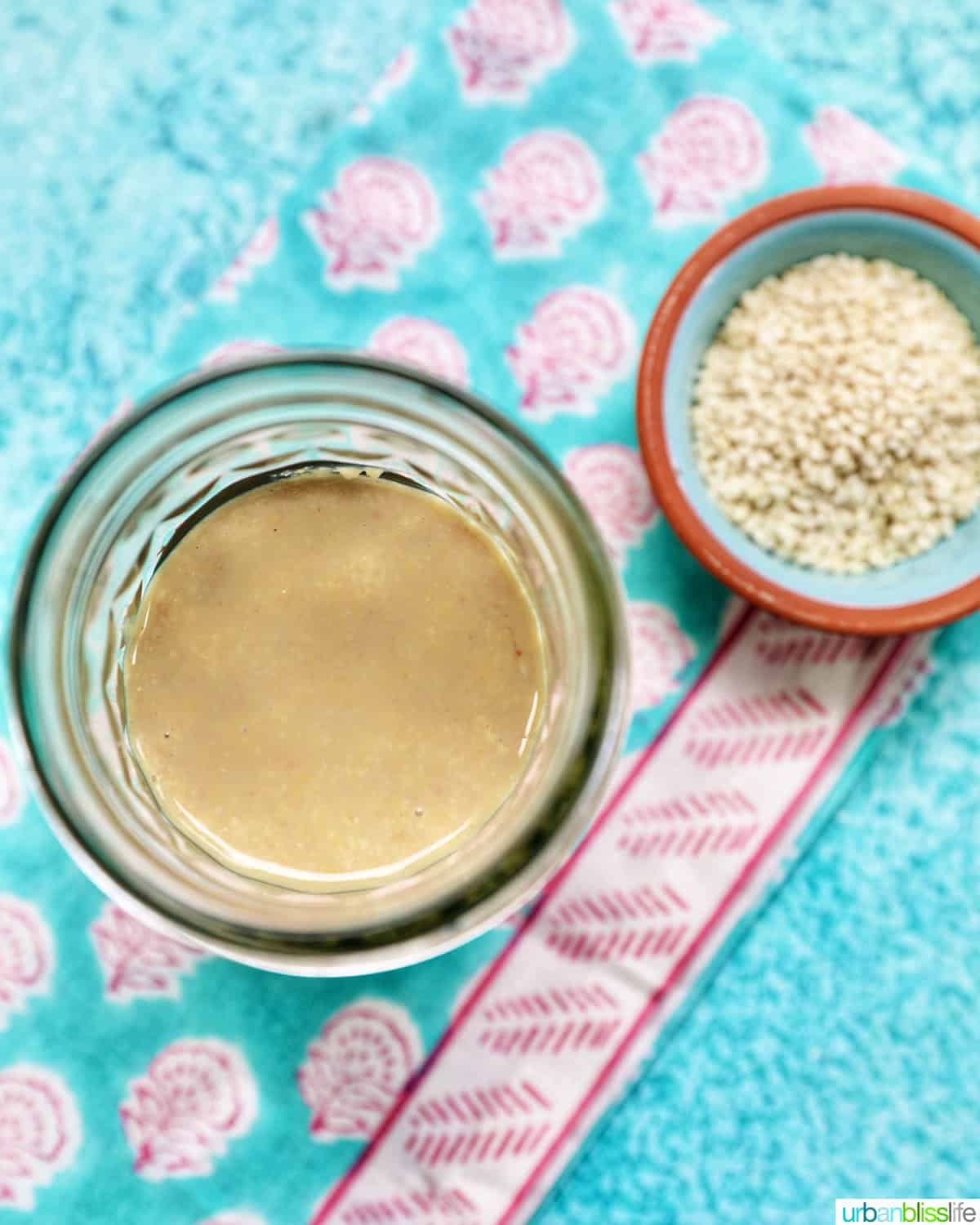 jar of homemade tahini with a small bowl of sesame seeds and a spoon.