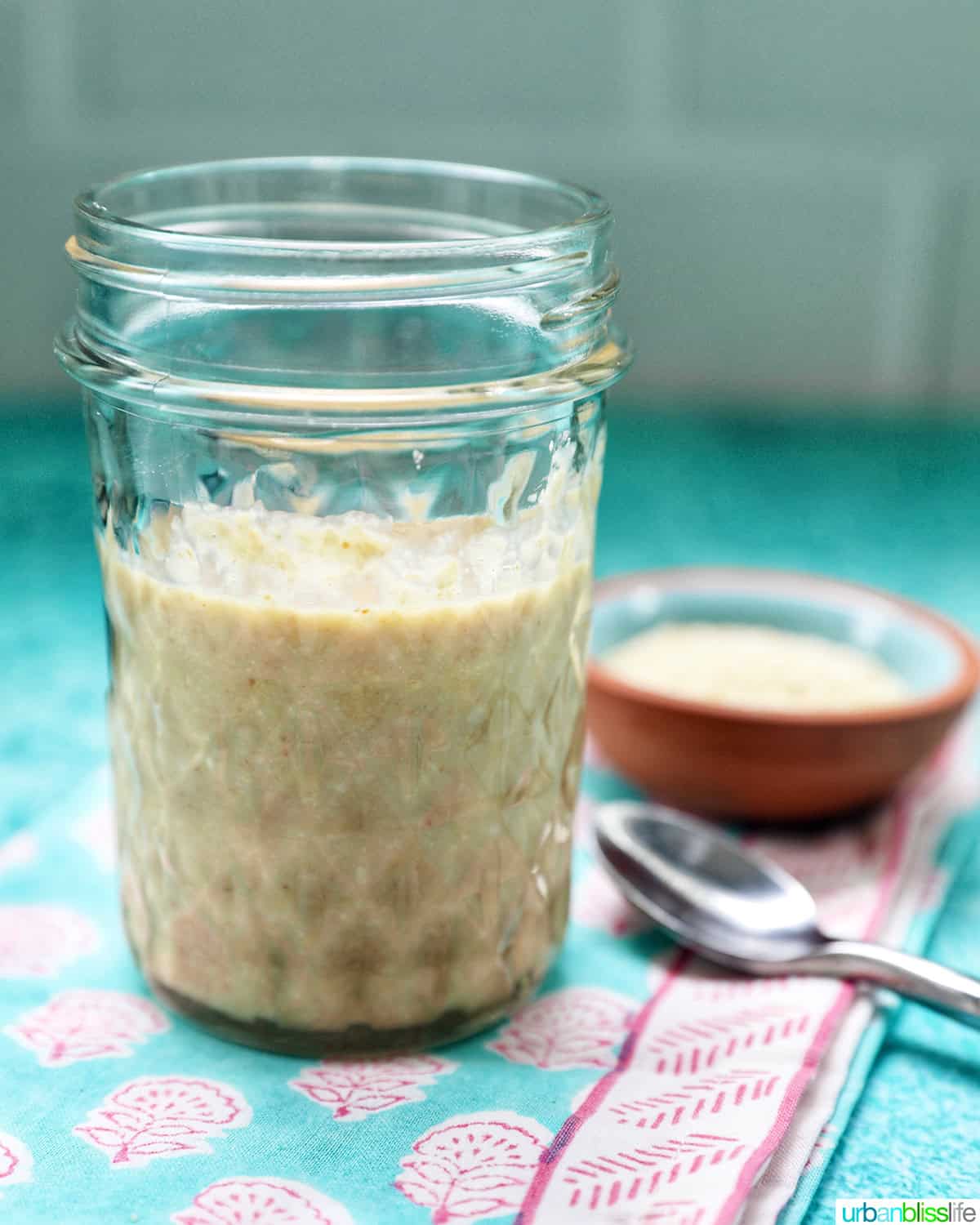 jar of homemade tahini with a small bowl of sesame seeds and a spoon.