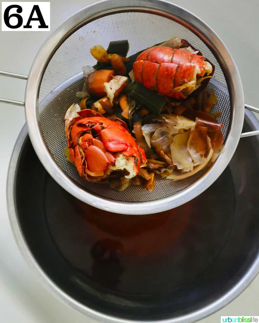 lobster and other seafood shells and vegetable scraps in a mesh strainer over a large pot of seafood stock.