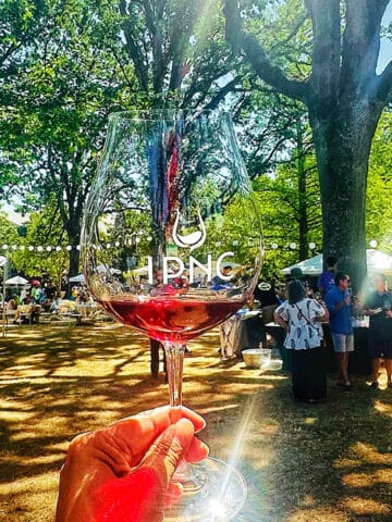 hand holding an IPNC wine glass against an outdoor wine tasting event.