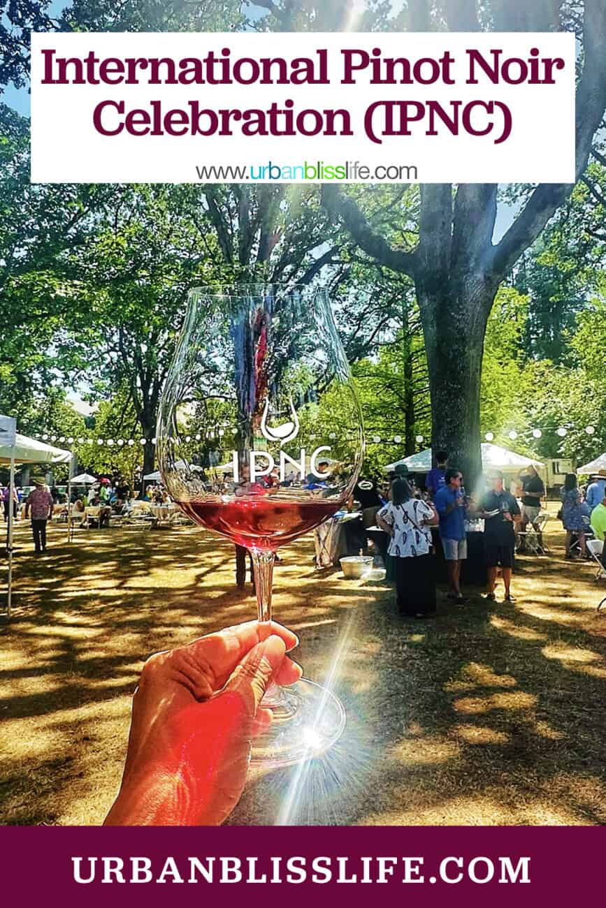 hand holding an IPNC wine glass against an outdoor wine tasting event.